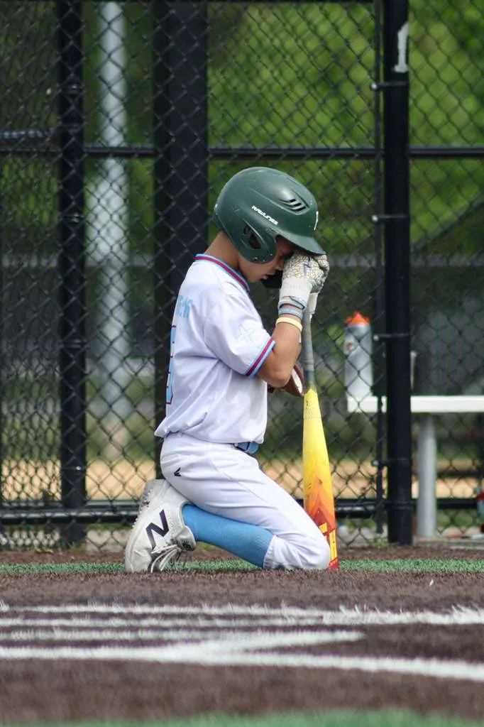 Young baseball player kneeling in prayer with bat in hand
